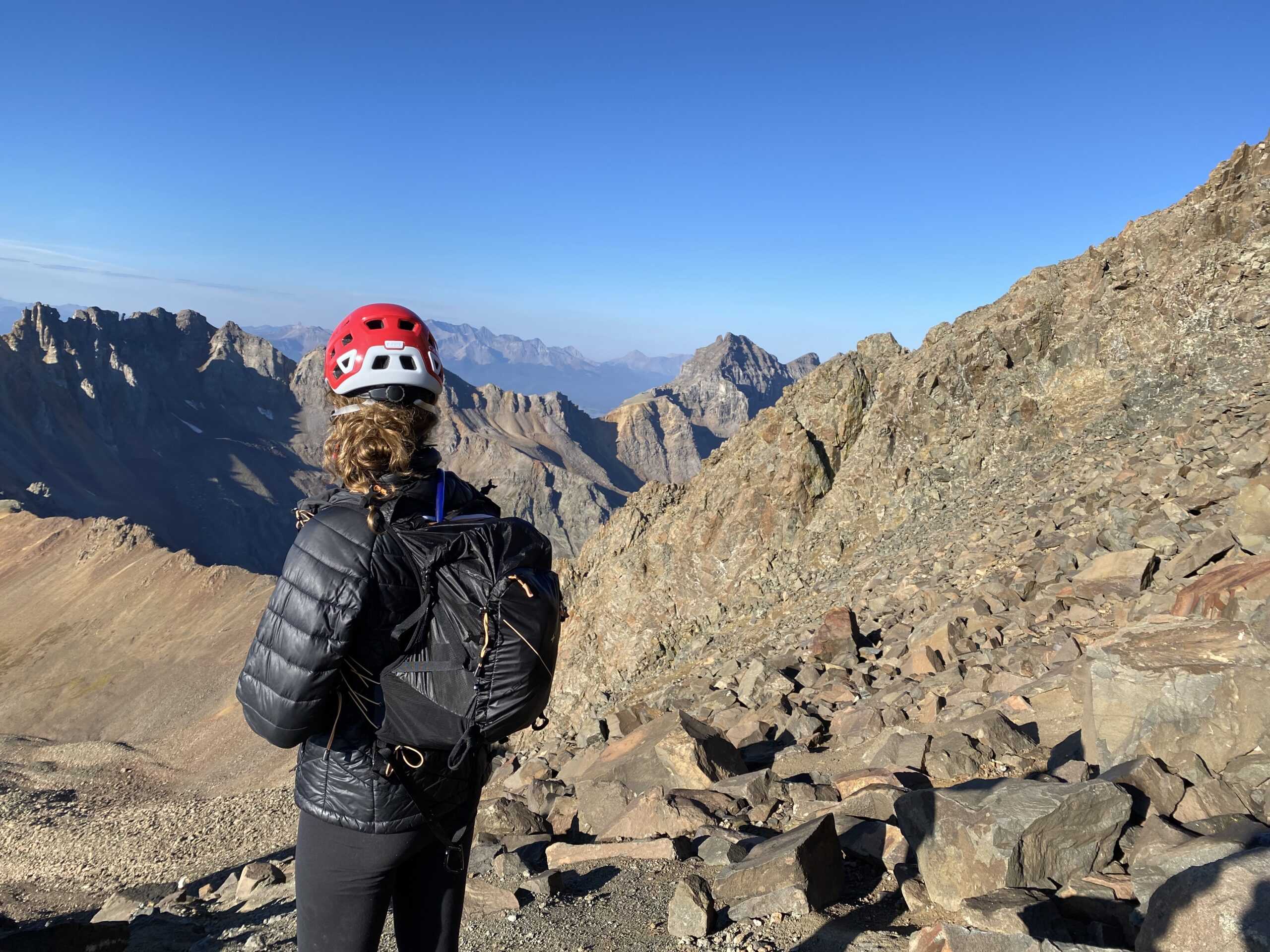 一个穿着黑色夹克，背着黑色背包，戴着红色登山帽的女人正在看山
